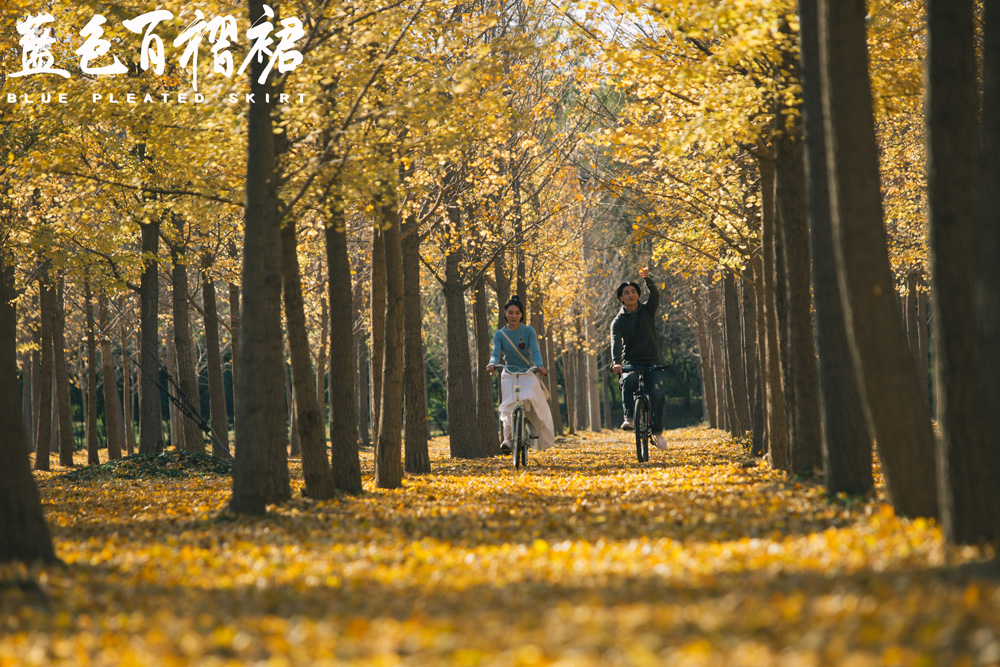蓝特儿和周洋在满是黄叶的林中骑车